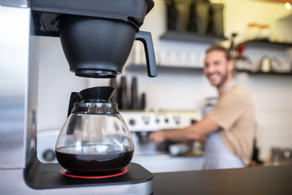 Cafeteira em destaque com um barista ao fundo.