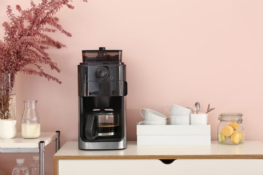 Cafeteira em um fundo rosa, com copos ao lado.