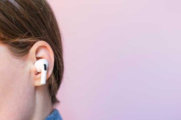 Mulher usando um fone branco intra-auricular em um fundo roxo claro.
