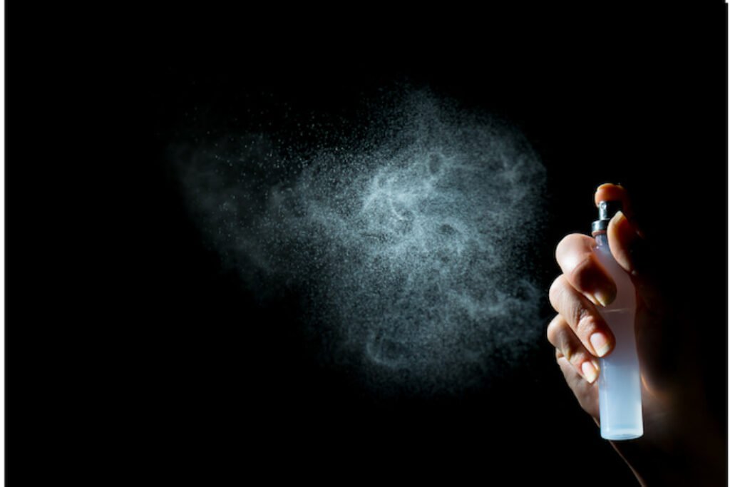 Perfume sendo borrifado em um fundo preto.