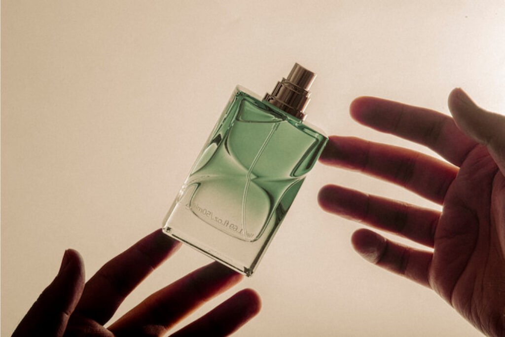 Sombras das mãos de uma pessoa manipulando um perfume de cor verde.