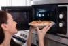 mulher colocando uma pizza no micro-ondas