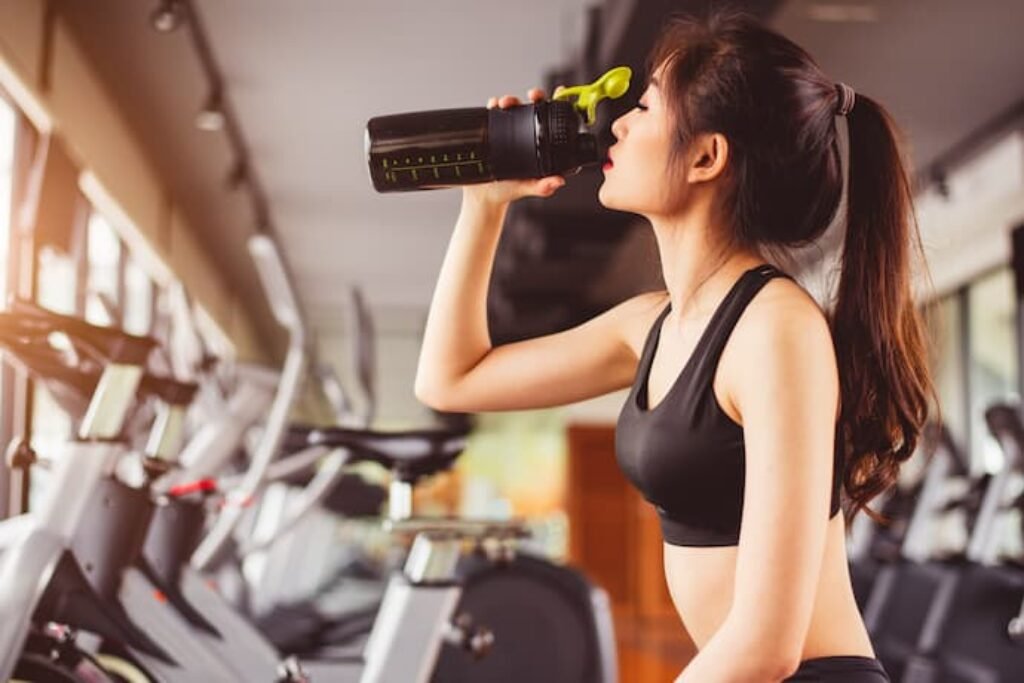 Uma garota tomando whey protein enquanto pedala na bicicleta ergométrica