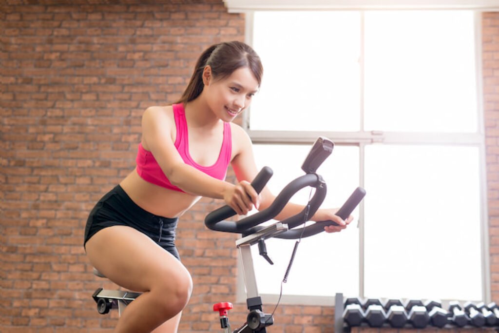 Mulher com trajes de academia pedalando em uma bicicleta ergométrica.