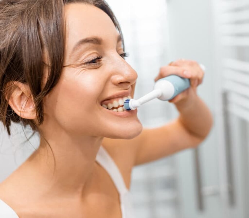 Uma mulher jovem escovando os dentes com a melhor escova de dente elétrica.