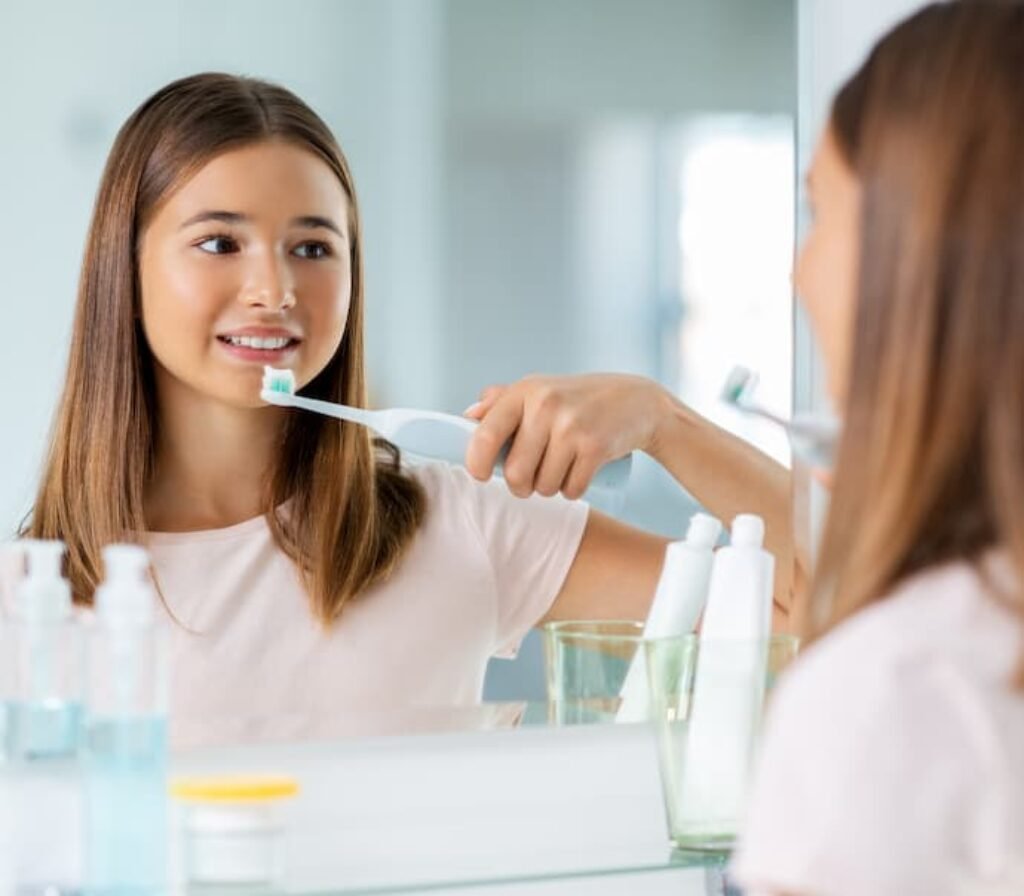 Uma garota se olha no espelho enquanto escova os dentes.