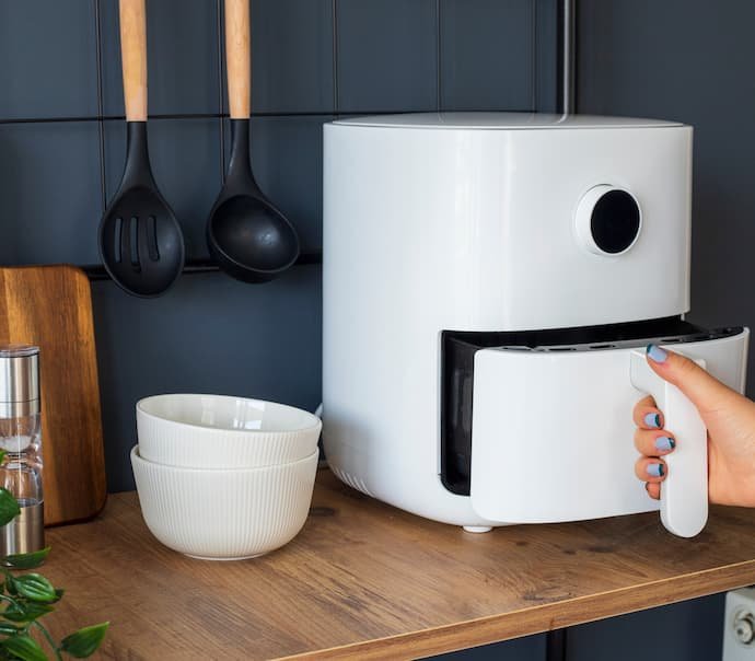 O melhor air fryer na cor branca em cima de uma mesa ao lado de duas tigelas.