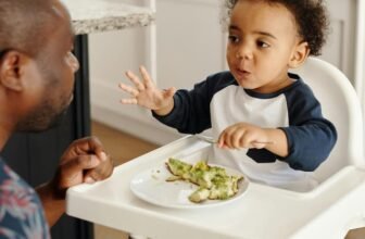 Um homem olhando uma bebê comendo e sentado em uma cadeira de alimentação