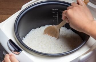 Uma pessoa mechendo o arroz que está dentro de uma panela elétrica.