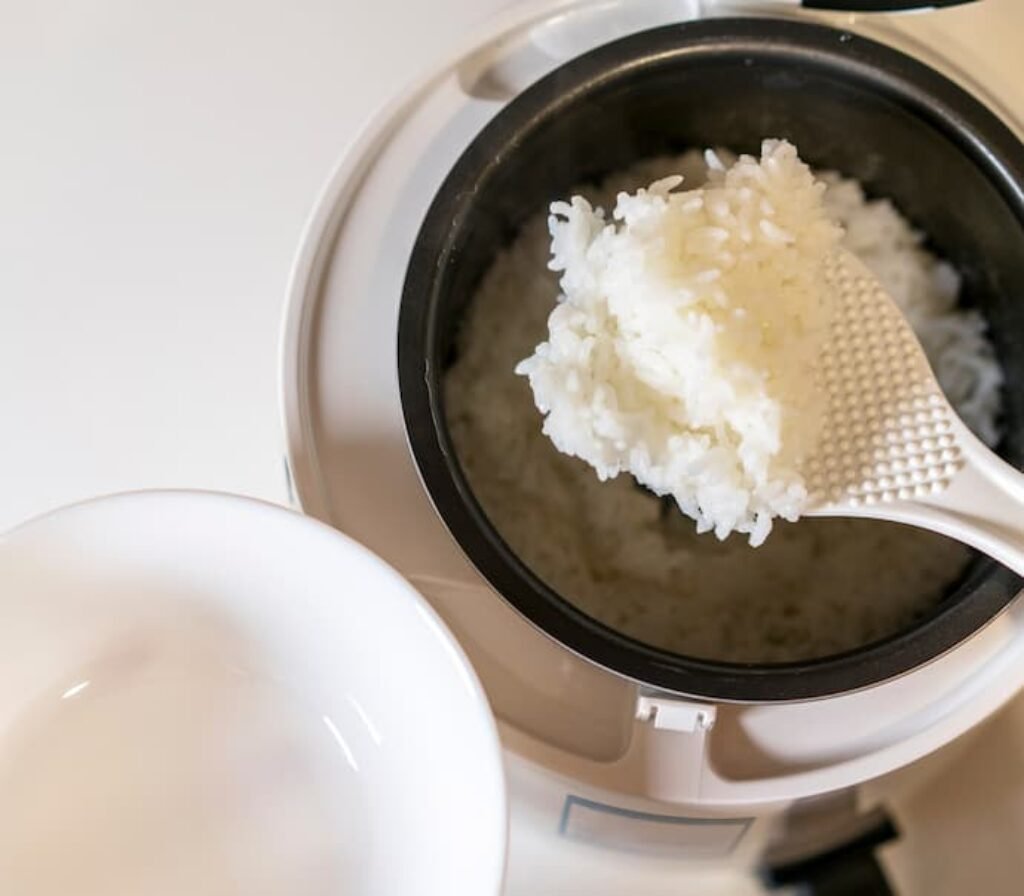 Uma pessoa tirando arroz de dentro de uma melhor panela de arroz elétrica pequena.