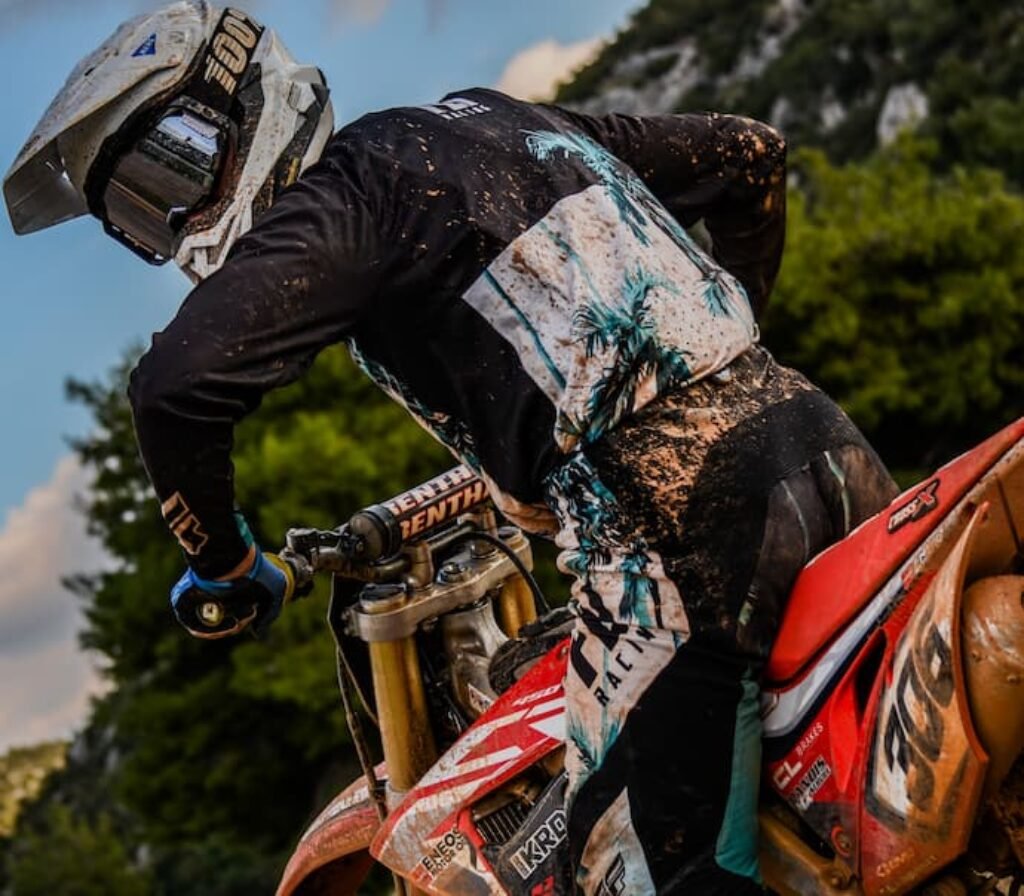 Um piloto de motocross em cima de uma moto e com um capacete aberto.