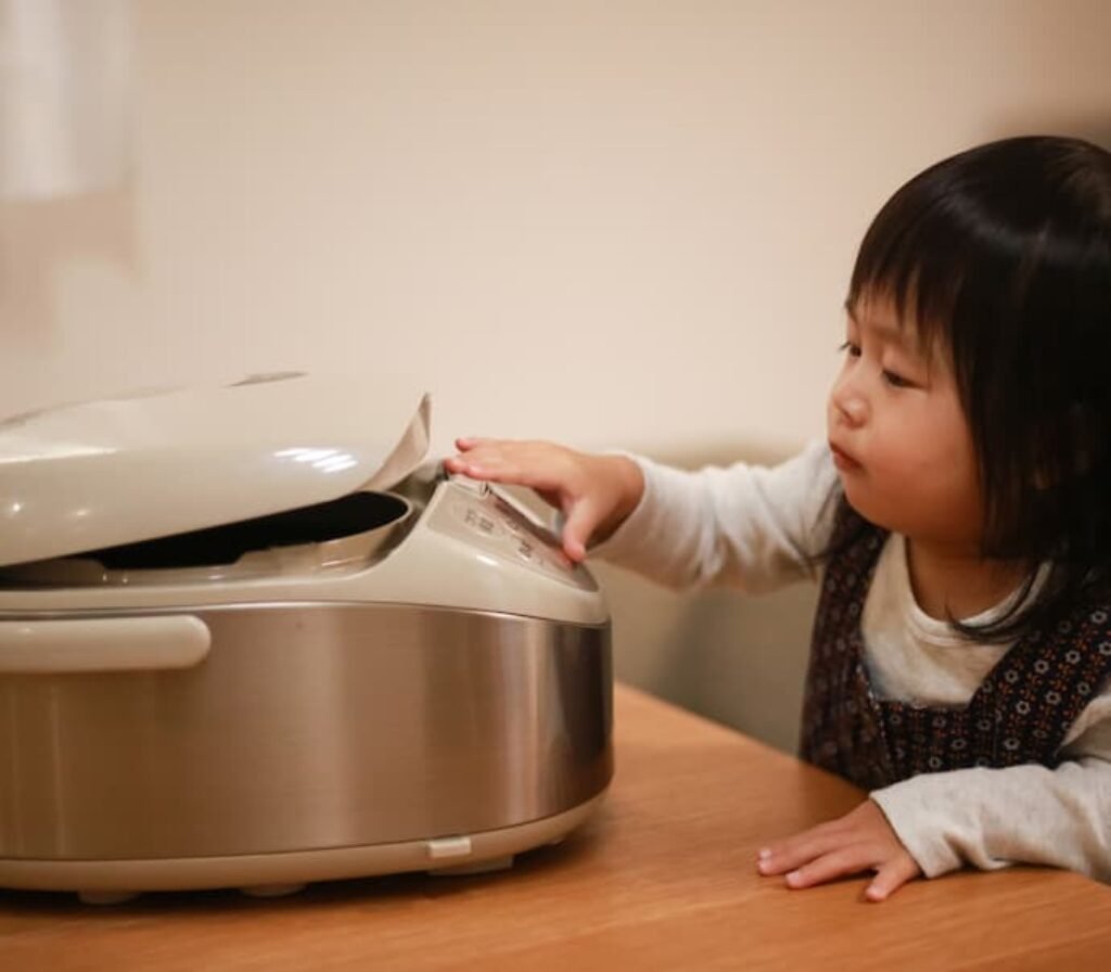 Uma criança apertando os botões de uma panela de arroz japonês elétrica.