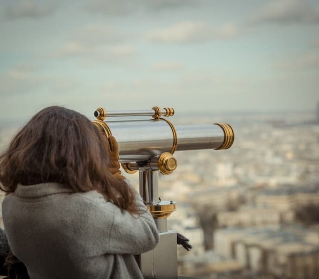 Uma mulher usando um telescópio grande em cima de um prédio.