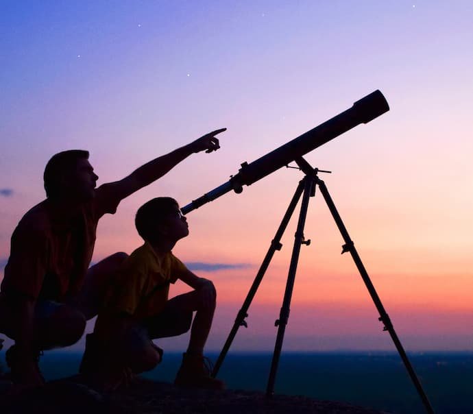 Uma pessoa olhando no telescópio e outra pessoa apontando o dedo para o céu