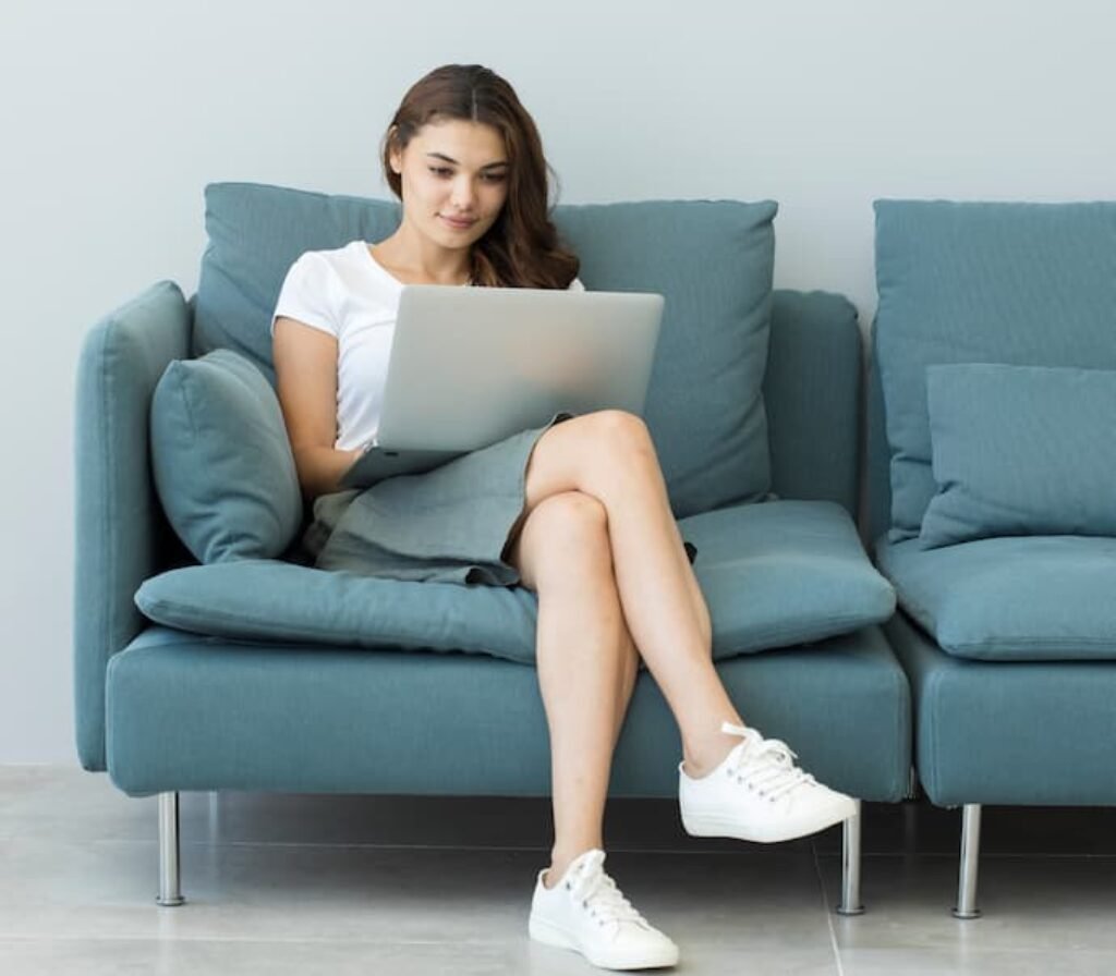 Uma mulher usando um laptop em um sofá.