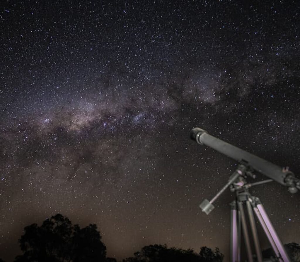 Um telescópio equatorial em um cenário noturno com muitas estrelas no céu.