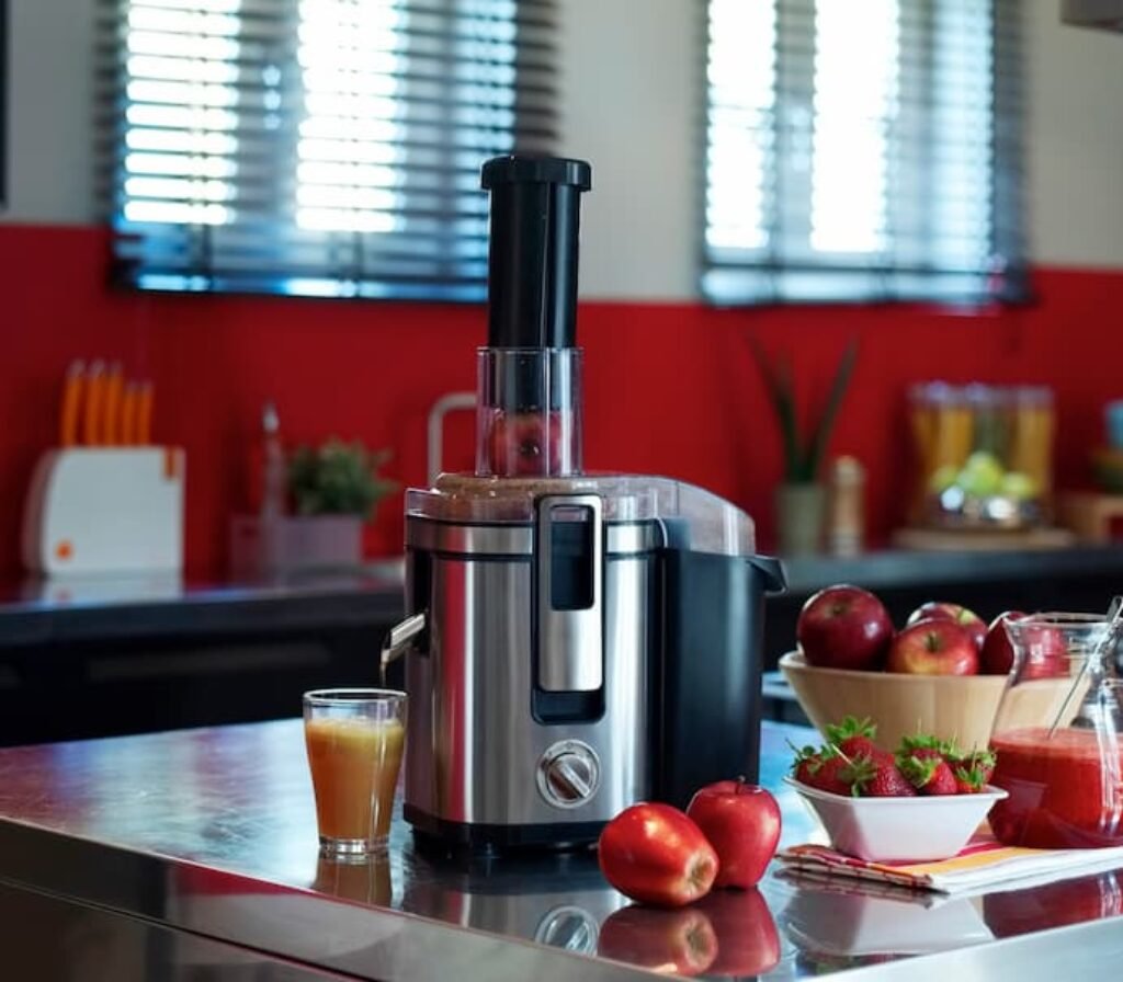 Um dos melhores espremedores de frutas com aço inox em cima de uma mesa, rodeado por frutas.