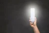 Pessoa segurando uma lâmpada led em um fundo cinza.