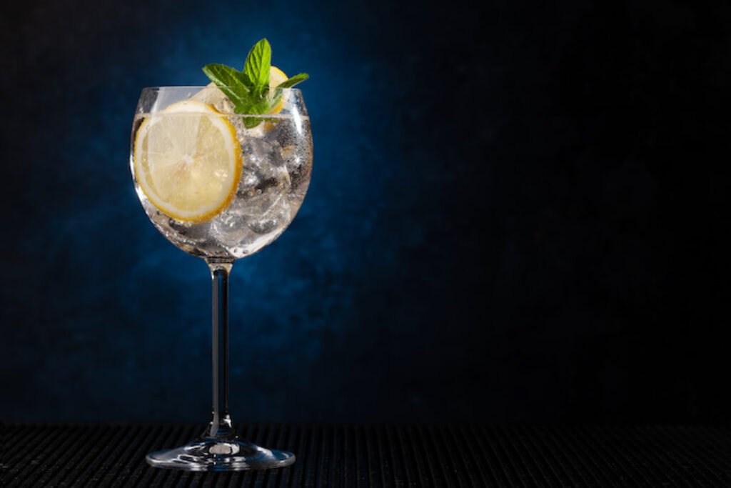 Taça de gin decorada com limão e folhas em um fundo azul.
