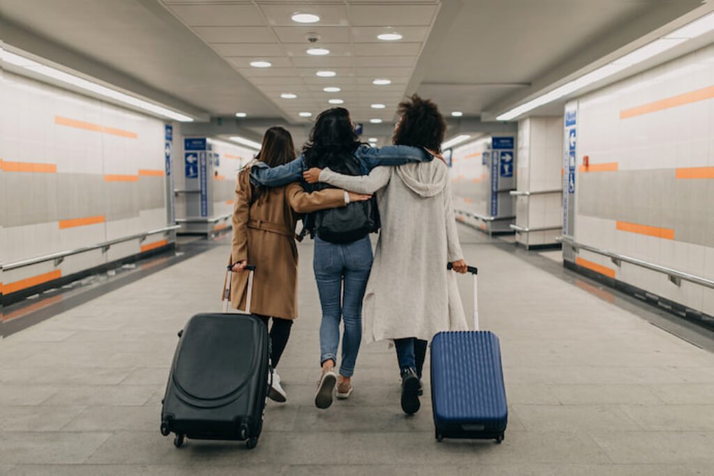 Três pessoas abraçadas no aeroporto. Duas carregam malas.