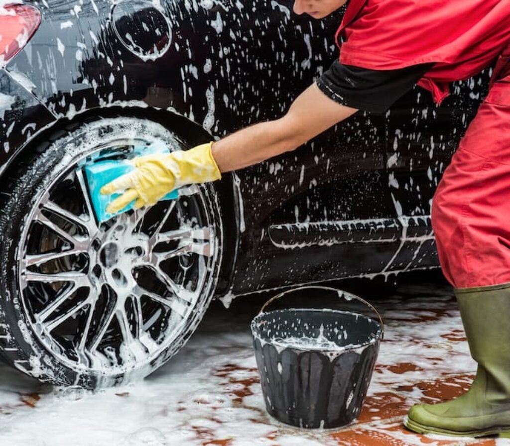 Um profissional lava um carro com shampoo e usa uma esponja.