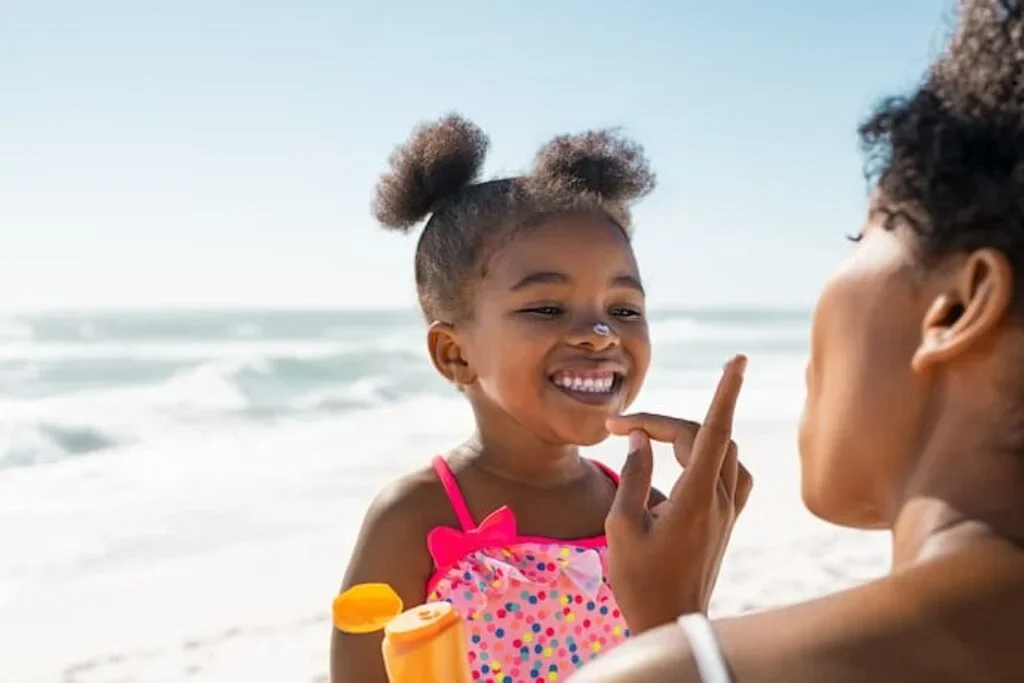 Uma mamãe colocando filtro solar na filhinha em uma praia.