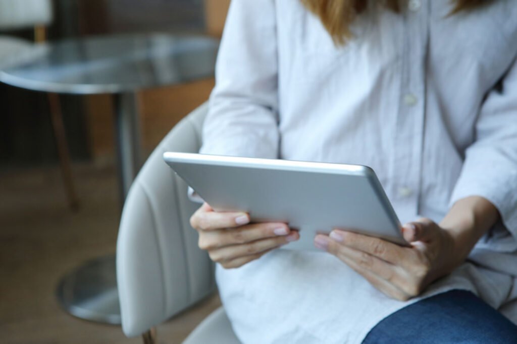 Um tablet com tela grande nãos mãos de uma pessoa sentada.