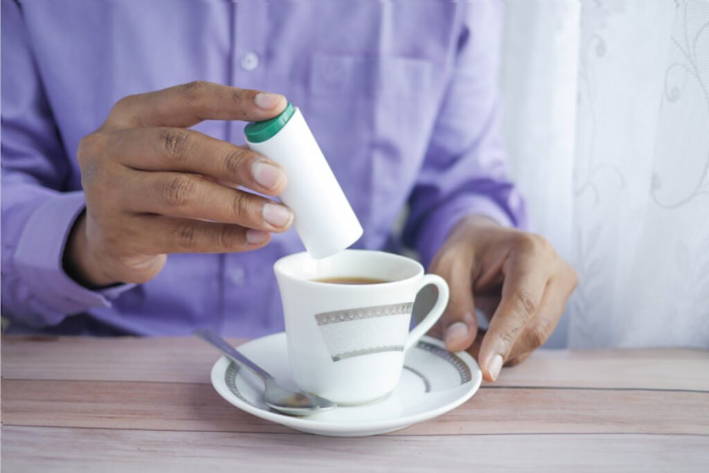 Pessoa colocando adoçante numa xícara de café.