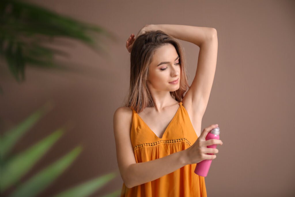 Mulher com blusa laranja passando desodorante aerosol.