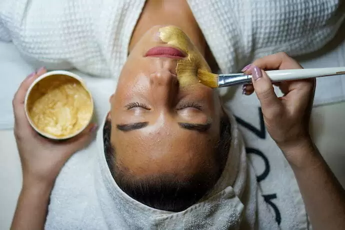 Profissional passando máscara facial em uma mulher.