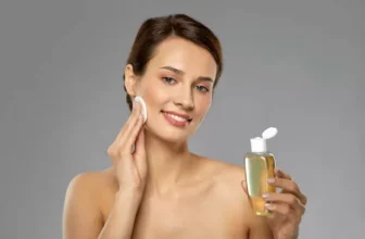 Mulher passando o melhor tônico para o rosto em um fundo cinza.
