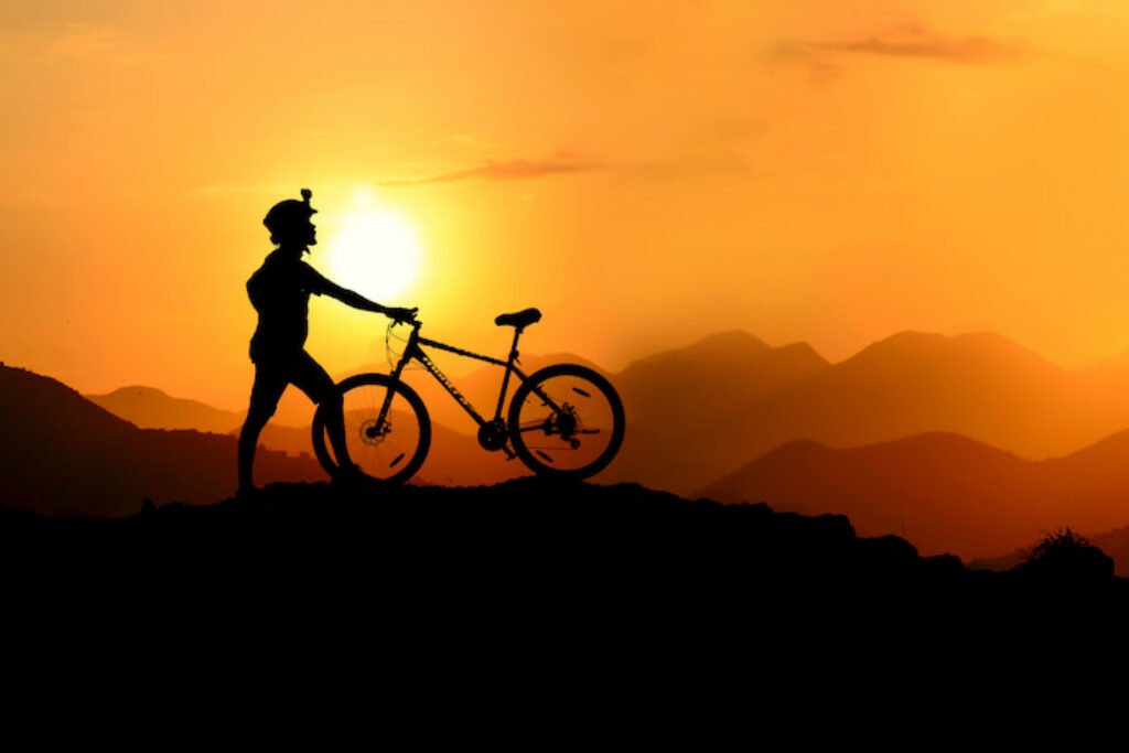 Silhueta de uma pessoa com bicicleta com o pôr do sol de fundo.
