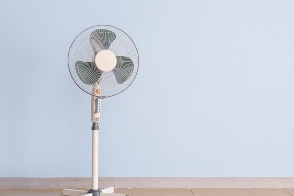 Ventilador grande desligado ao lado de uma parede azul.