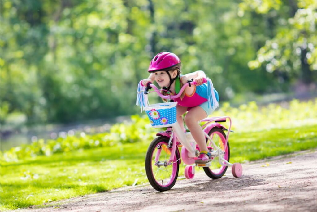 Criança de equipamento rosa andando de bicicleta infantil.