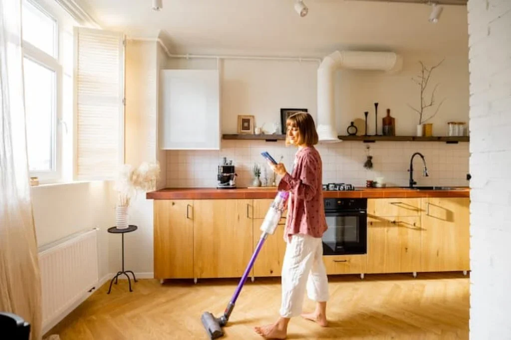 Uma mulher utilizando um aspirador de pó de 2000 Watts para aspirar o chão de uma cozinha.
