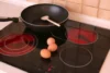 Em cima de um cooktop elétrico hé 3 ovos e uma frigideira.