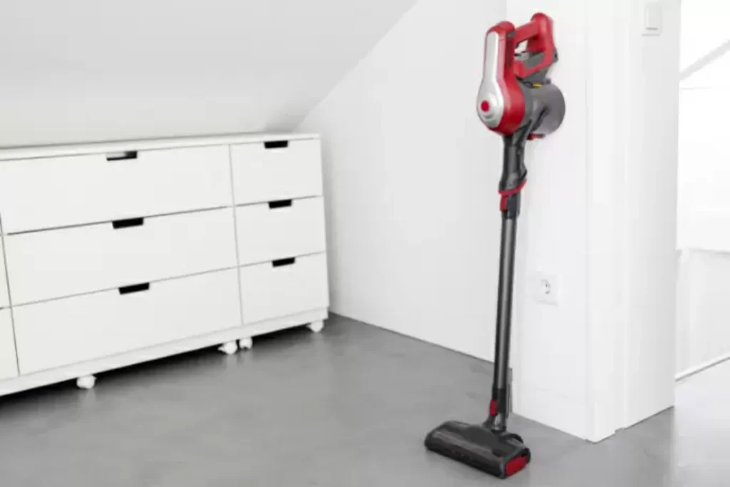 Um aspirador der pó vertical ao lado de uma tomada em um quarto.