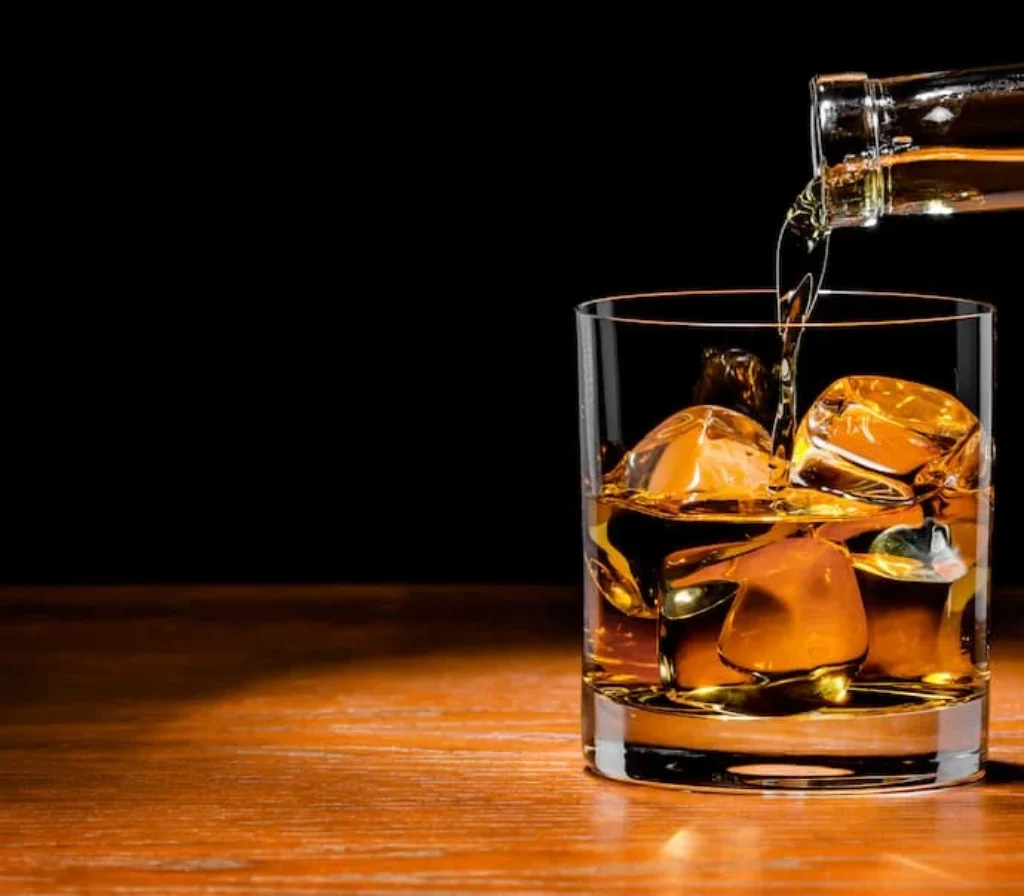 Uma garrafa enchendo um copo com bourbon.