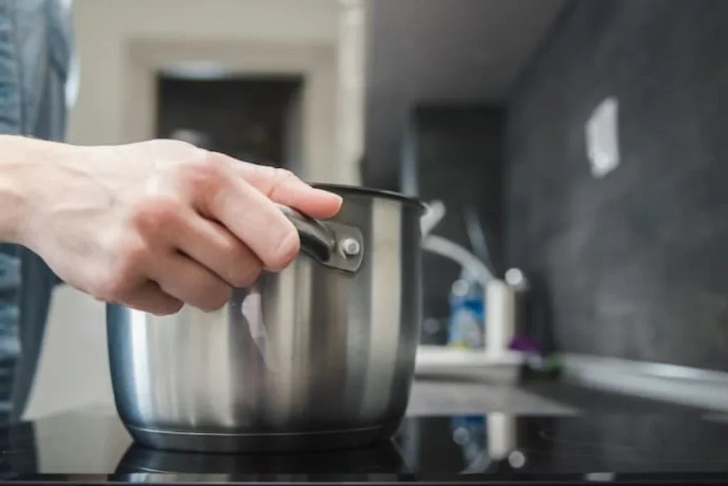 Uma pessoa retirando uma panela do melhor cooktop 4 bocas.