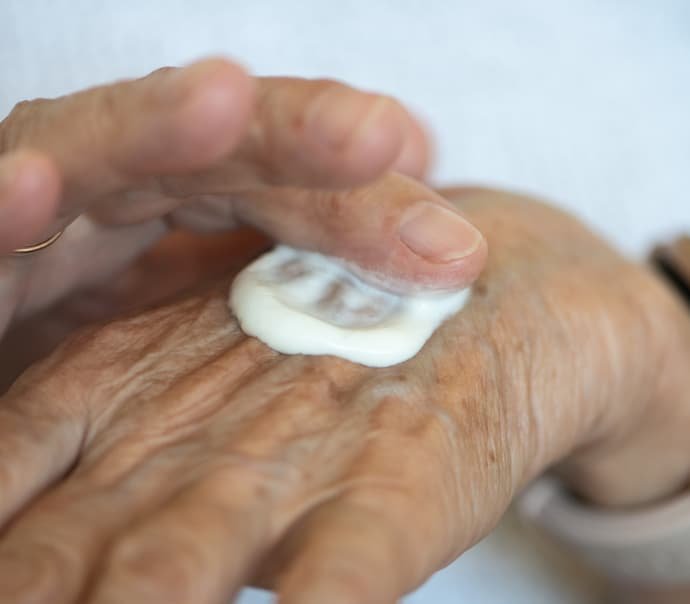 Uma pessoa idosa passando o melhor creme para mãos envelhecidas.