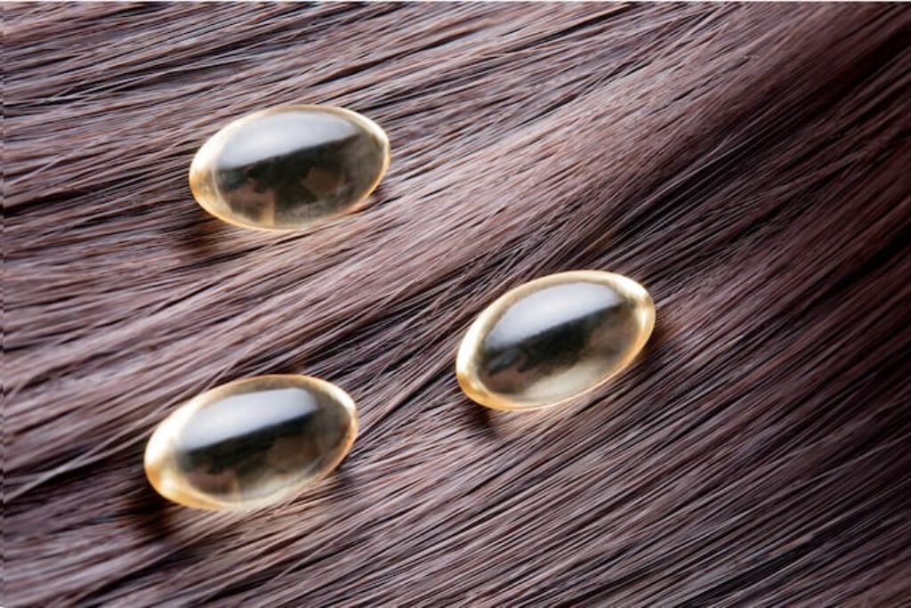 Cápsulas gelatinosas de vitamina próximas ao cabelo.