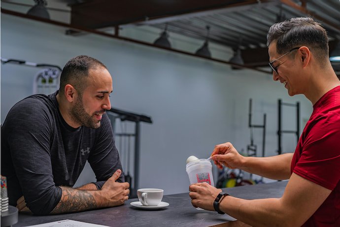 Dois homens conversando enquanto um deles prepara whey.