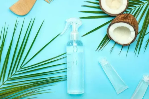 Frasco de tônico capilar em um fundo azul ciano com folhas e cocos ao redor.