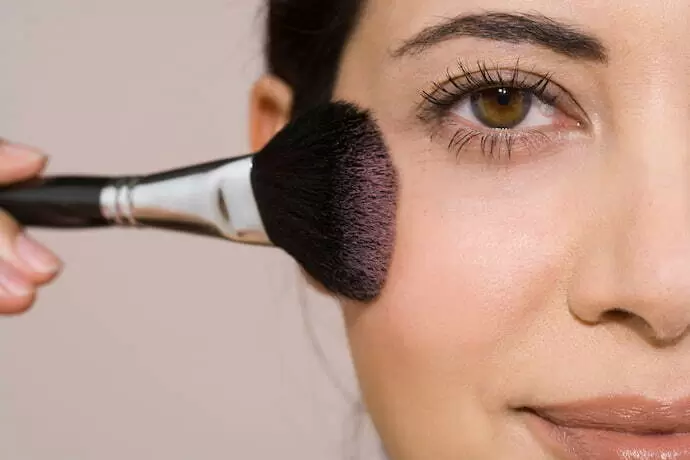 Mulher passando blush no rosto.