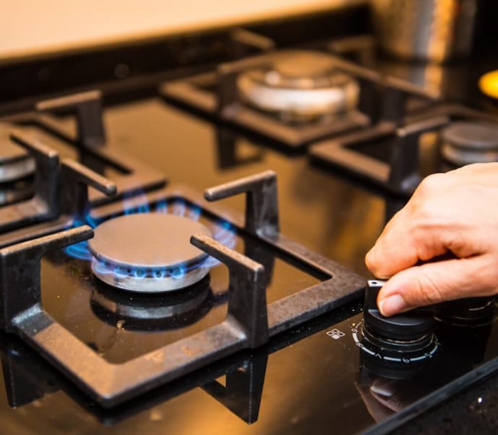 Uma pessoa regulando a temperatura em um melhor fogão 4 bocas de titanium com mesa de vidro.