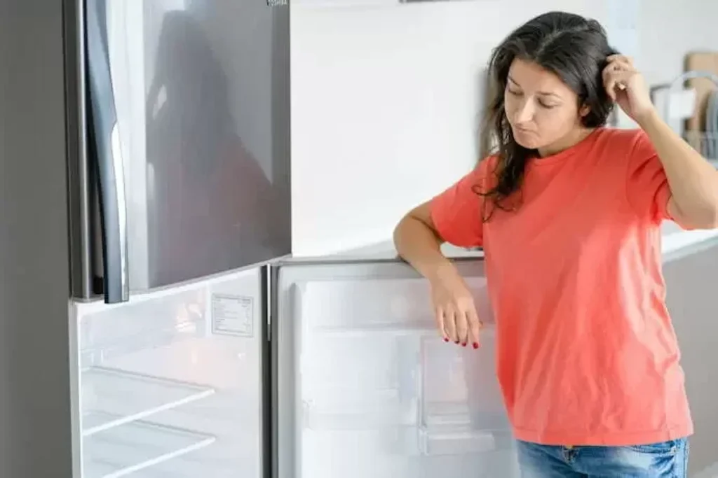 Uma mulher abrindo uma porta de uma geladeira vazia.