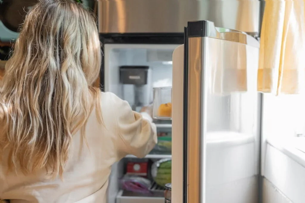 Uma mulher retirando um alimento de dentro de uma geladeira.