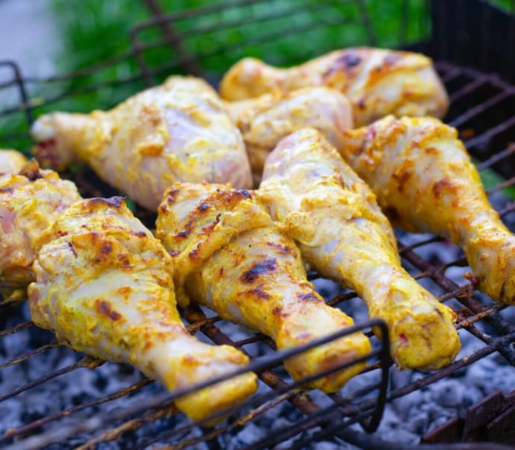 Coxas de frango sendo assadas em uma grelha de uma das melhores churrsaqueiras a carvão portáteis.