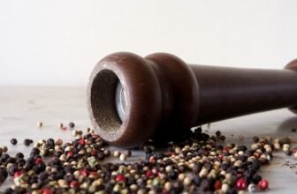 Um dos melhores moedores de pimenta de madeira e alguns grãos de pimenta espalhados na mesa.