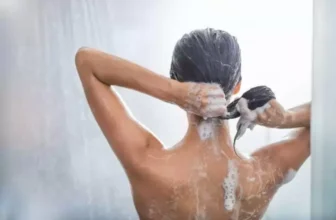 Mulher passando shampoo no cabelo no banho.